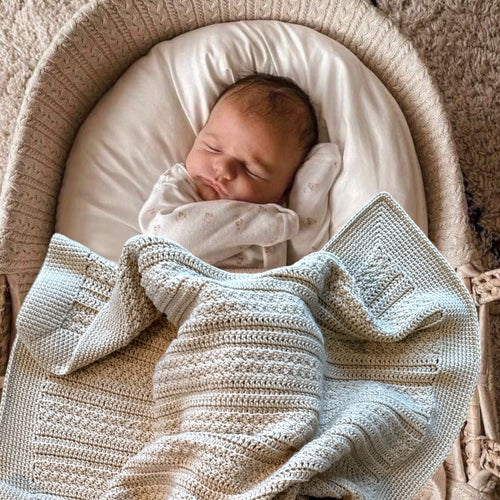 Newborn baby sleeping in a bassinet with a textured blanket